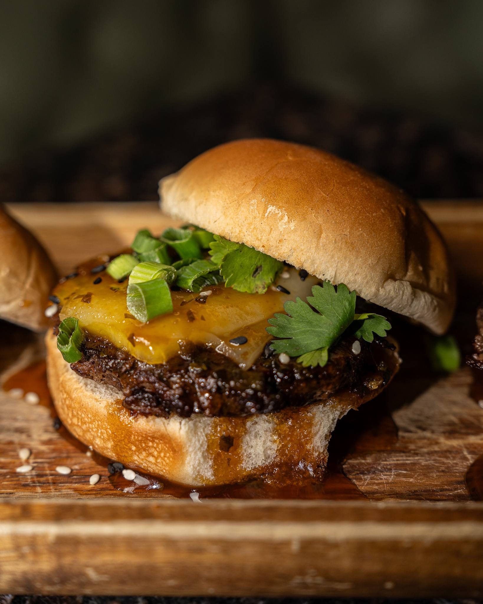 Close-up of a wagyu slider with grilled pineapple, scallions and sesame on a sweet roll.