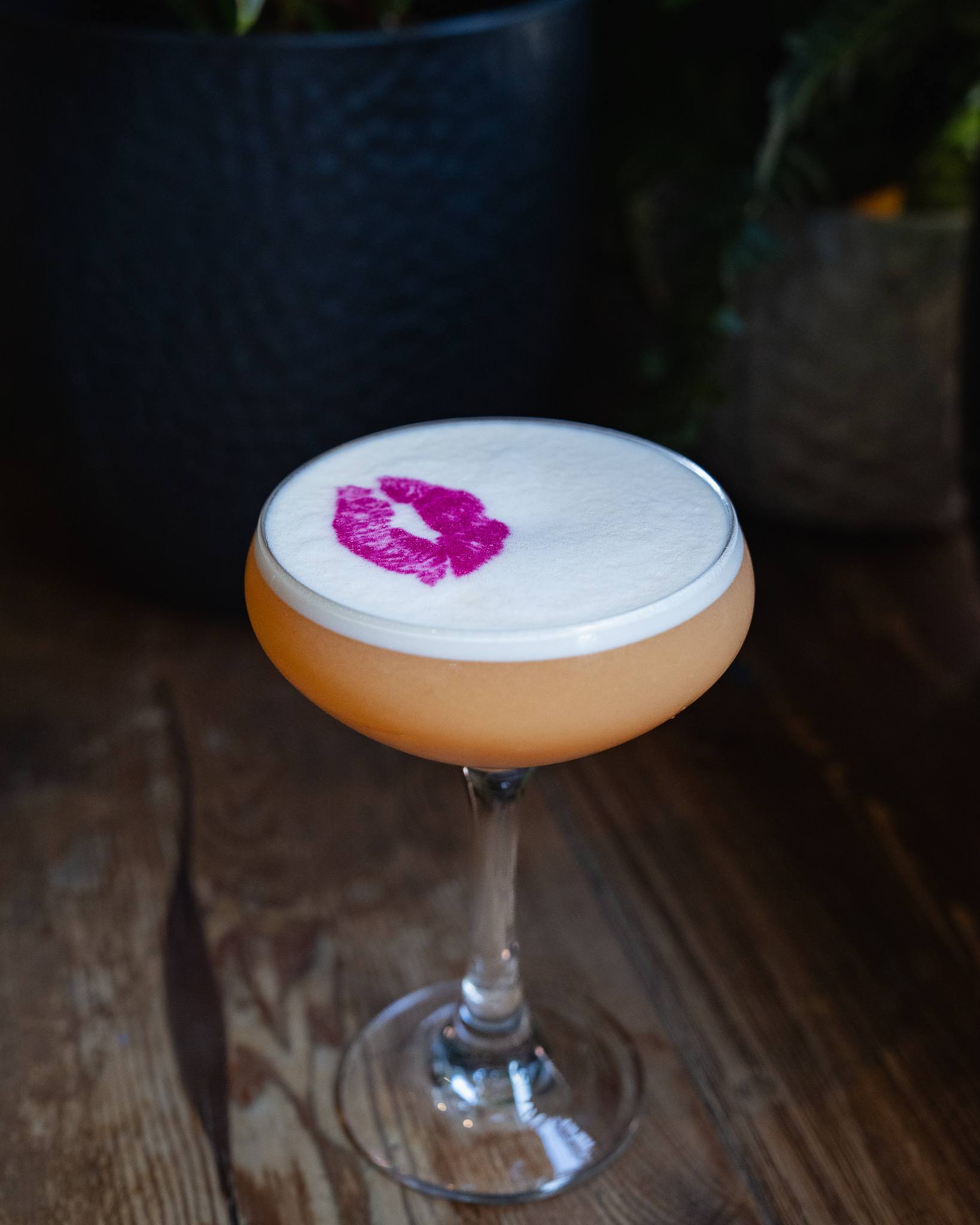 A peach-coloured cocktail in a coupe, its white foam printed with a pink lipstick kiss.