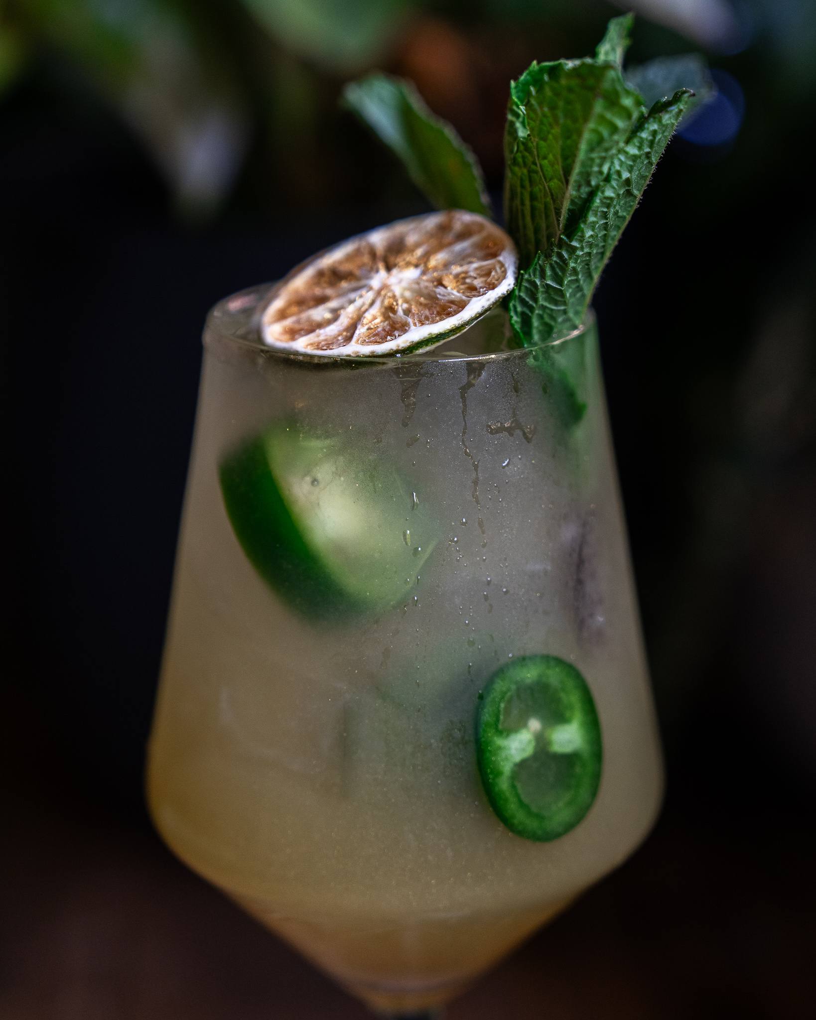 Close-up of a frosted glass with jalapeño slices, dried lime and mint.