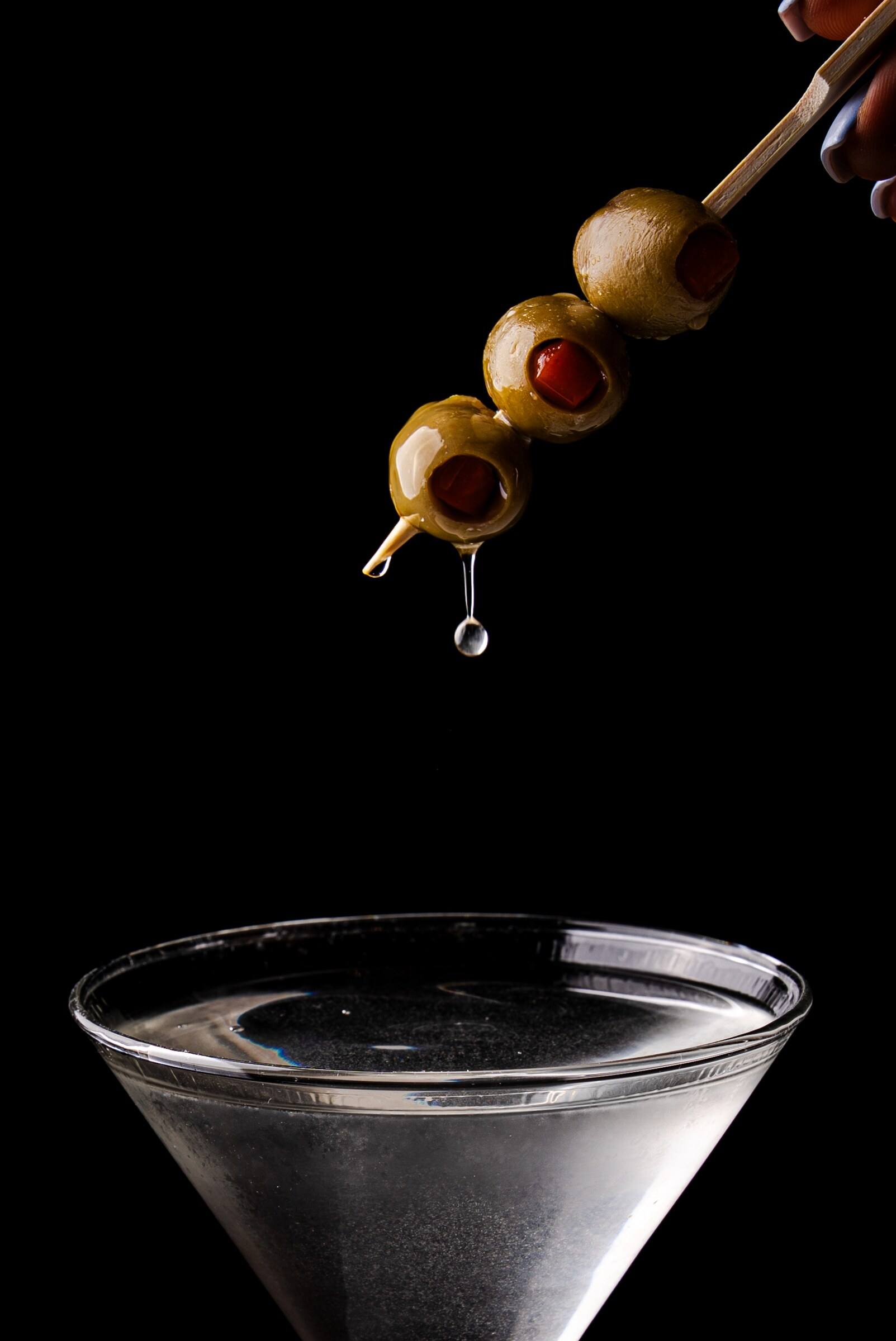Three pimento-stuffed olives drip above the rim of a chilled martini.