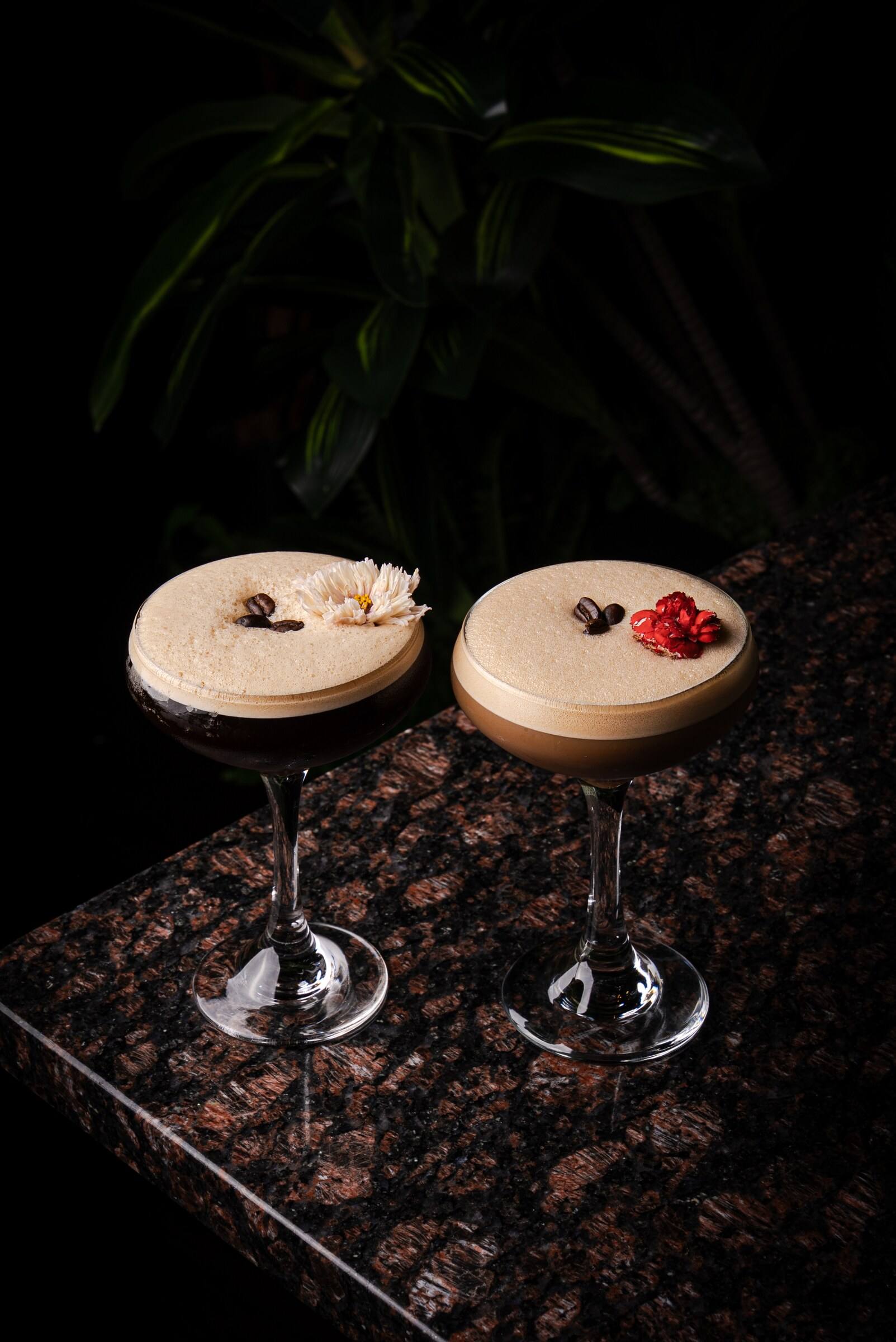 Two espresso martinis in coupe glasses topped with flowers and coffee beans.